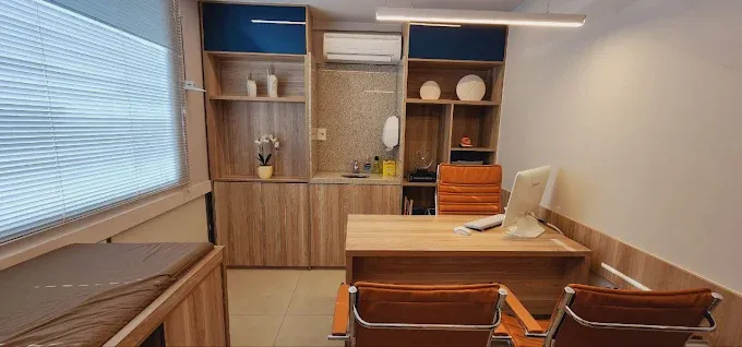Consultório com poltronas confortáveis e computador, ideal para atendimentos prolongados e escuta atenta.