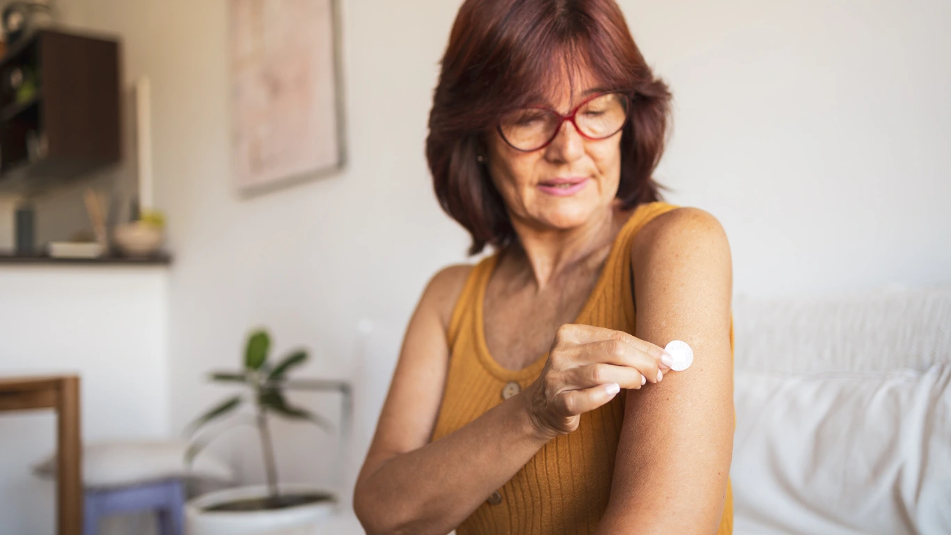 Mulher aplicando adesivo hormonal no braço como parte do tratamento médico