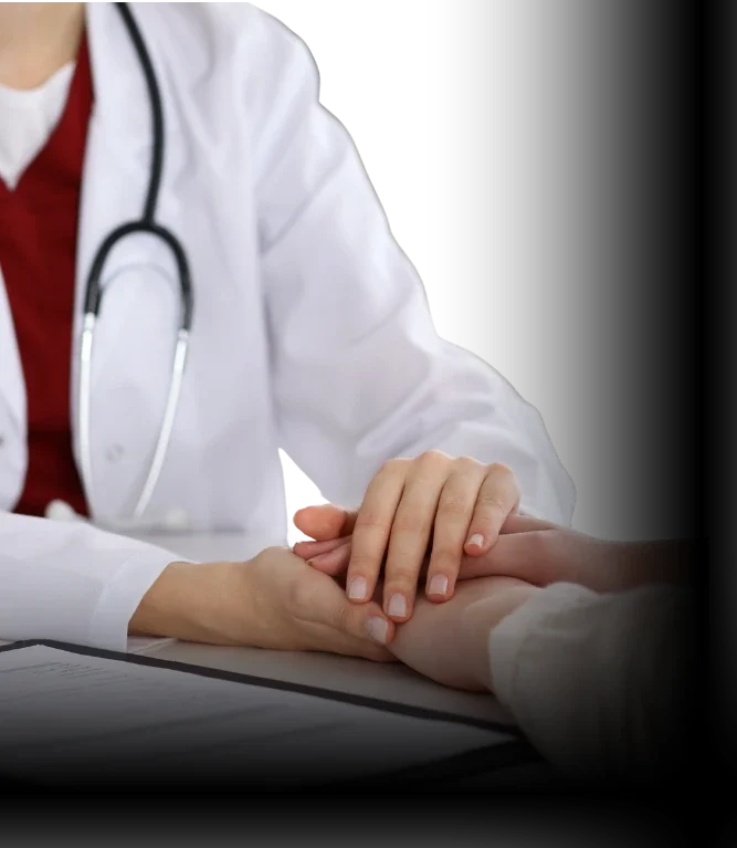 Médica de família digitando e segurando a mão de uma paciente, demonstrando acolhimento e cuidado humanizado durante a consulta.