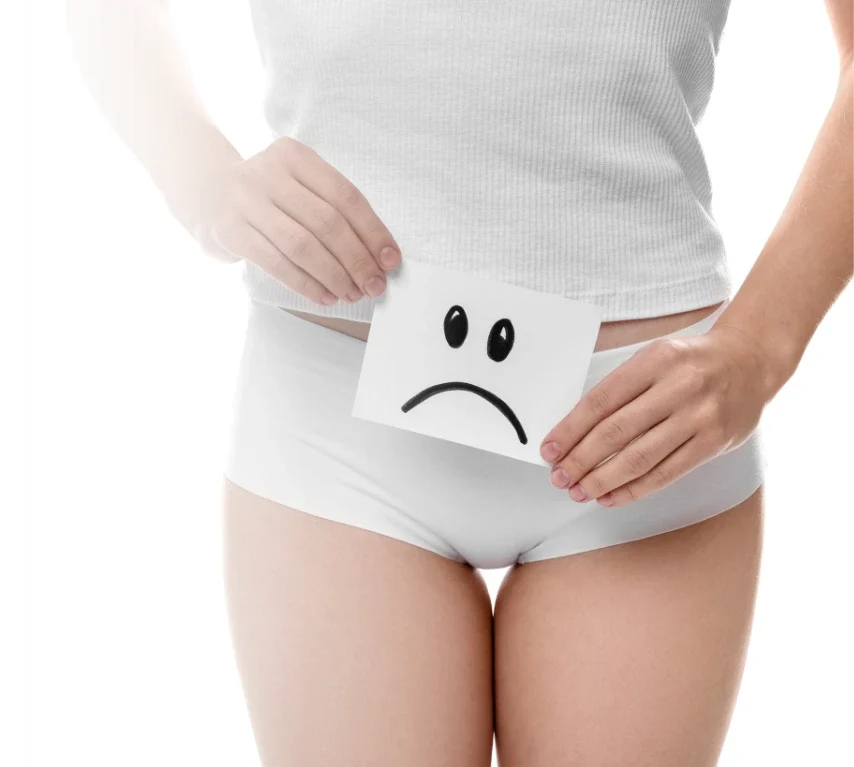 Mulher segurando um cartão com rosto triste sobre a região íntima, representando desconfortos e questões ligadas à sexualidade feminina.