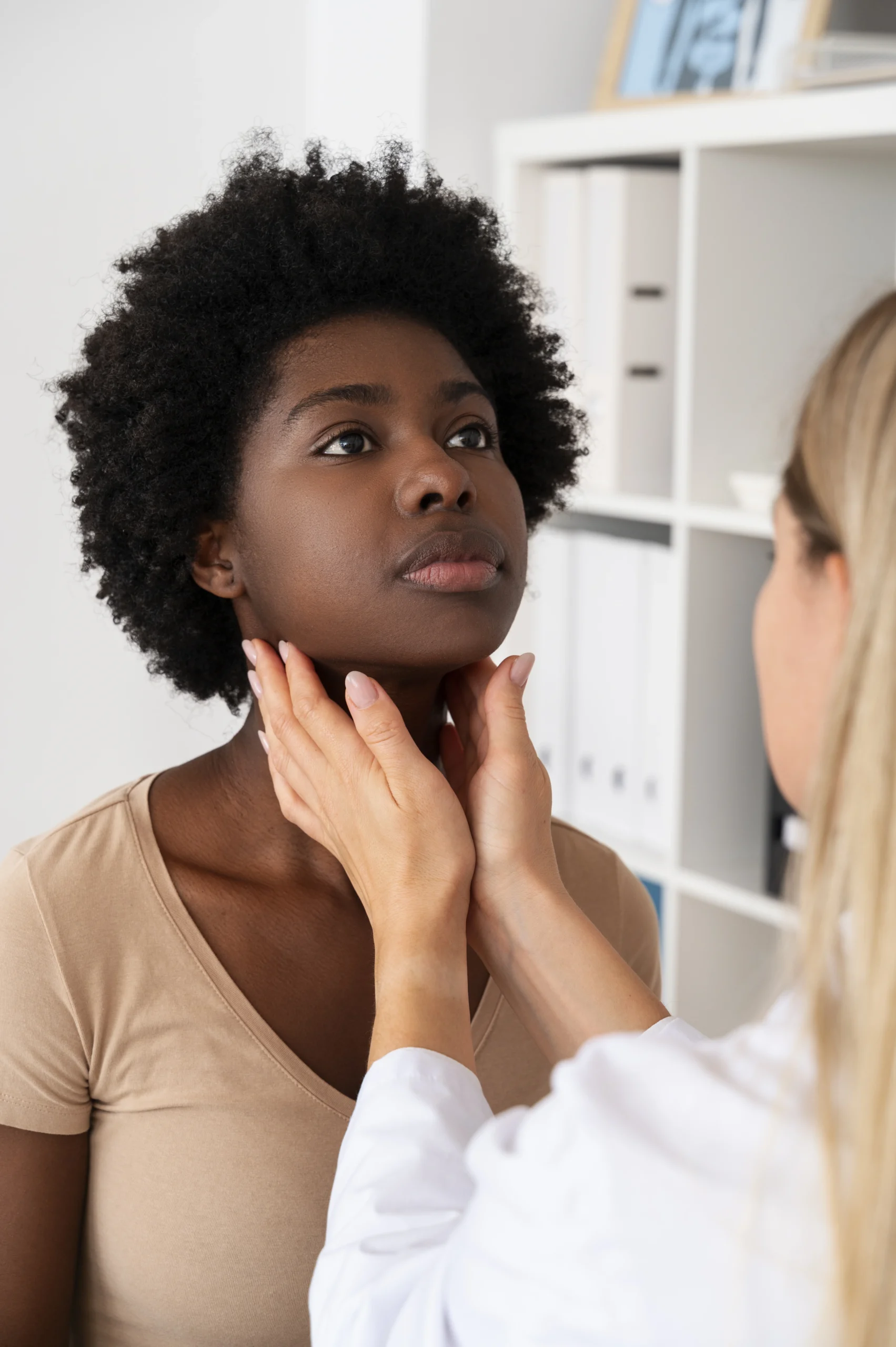 Médica examinando a tireoide de uma mulher durante consulta, palpando a região do pescoço para avaliar possíveis alterações.